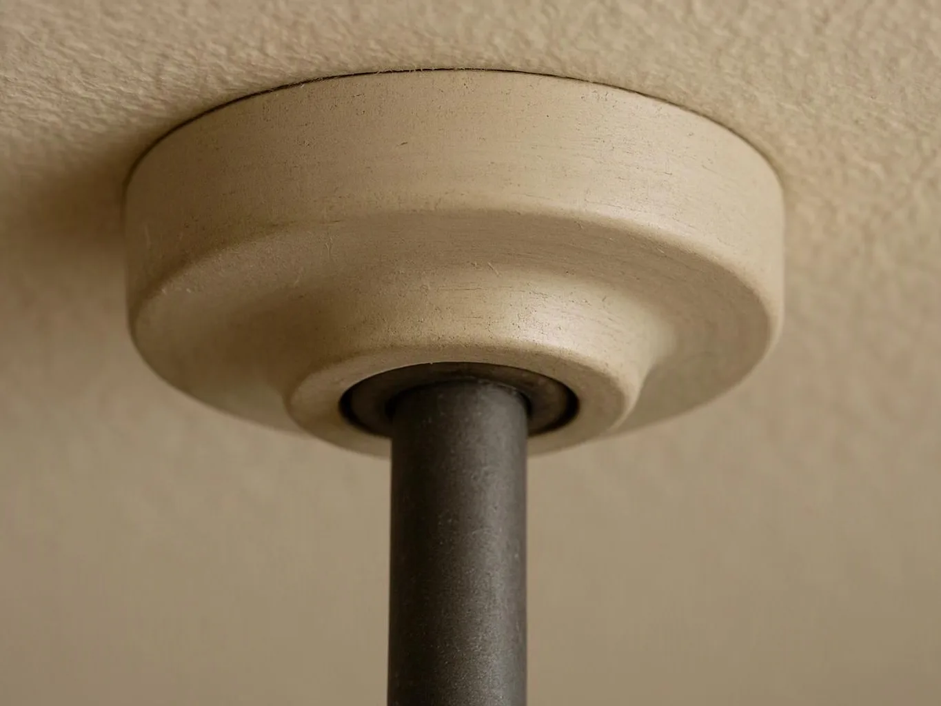 Close-up of a beige ceiling fixture with a dark metal rod against a textured wall and ceiling