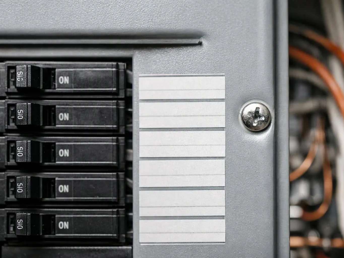 Close-up of a breaker panel with five black switches, a blank label strip, and visible wires inside the box