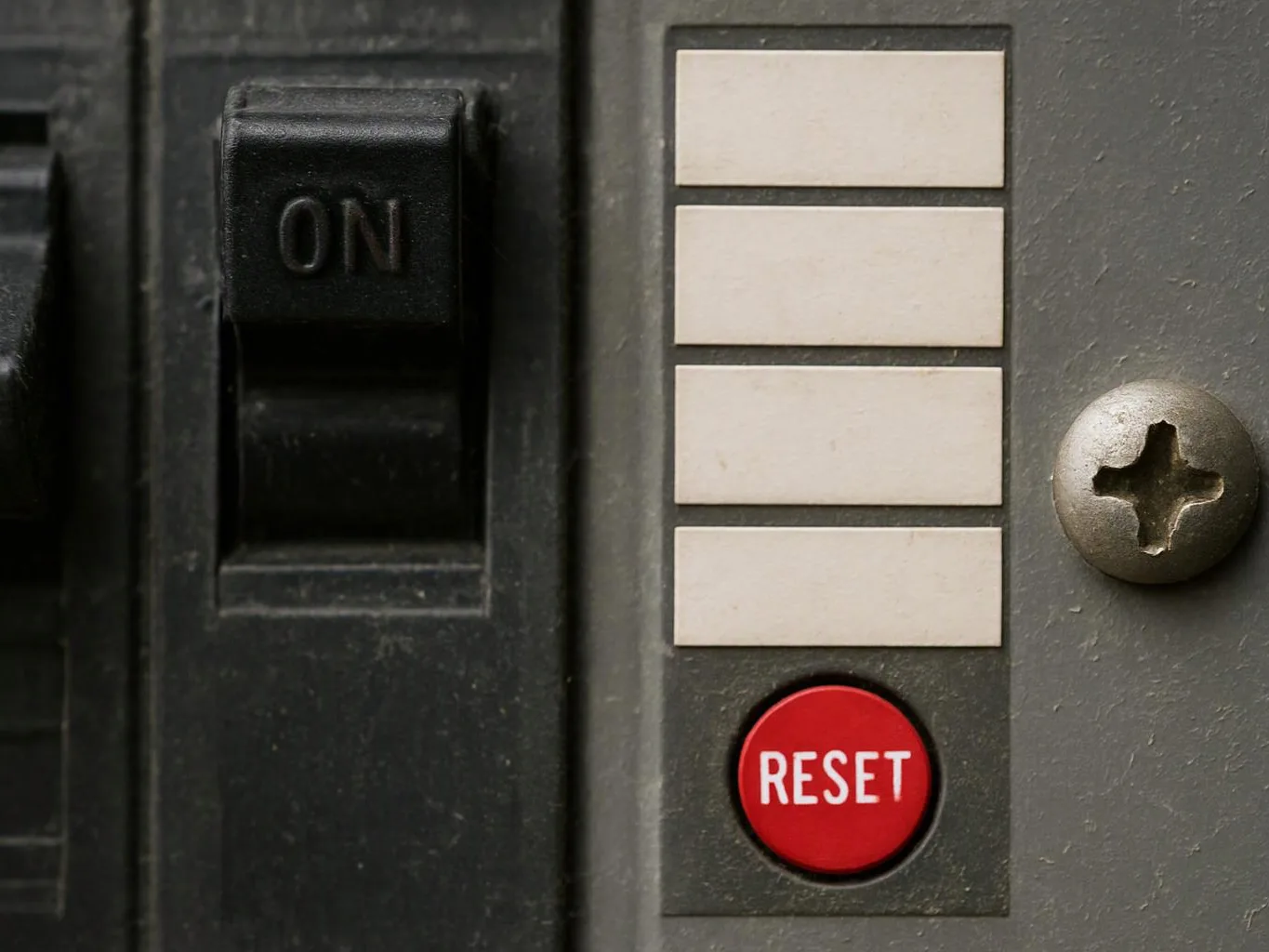 Close-up of a gray electrical breaker panel with an on switch, blank labels, and a red RESET button
