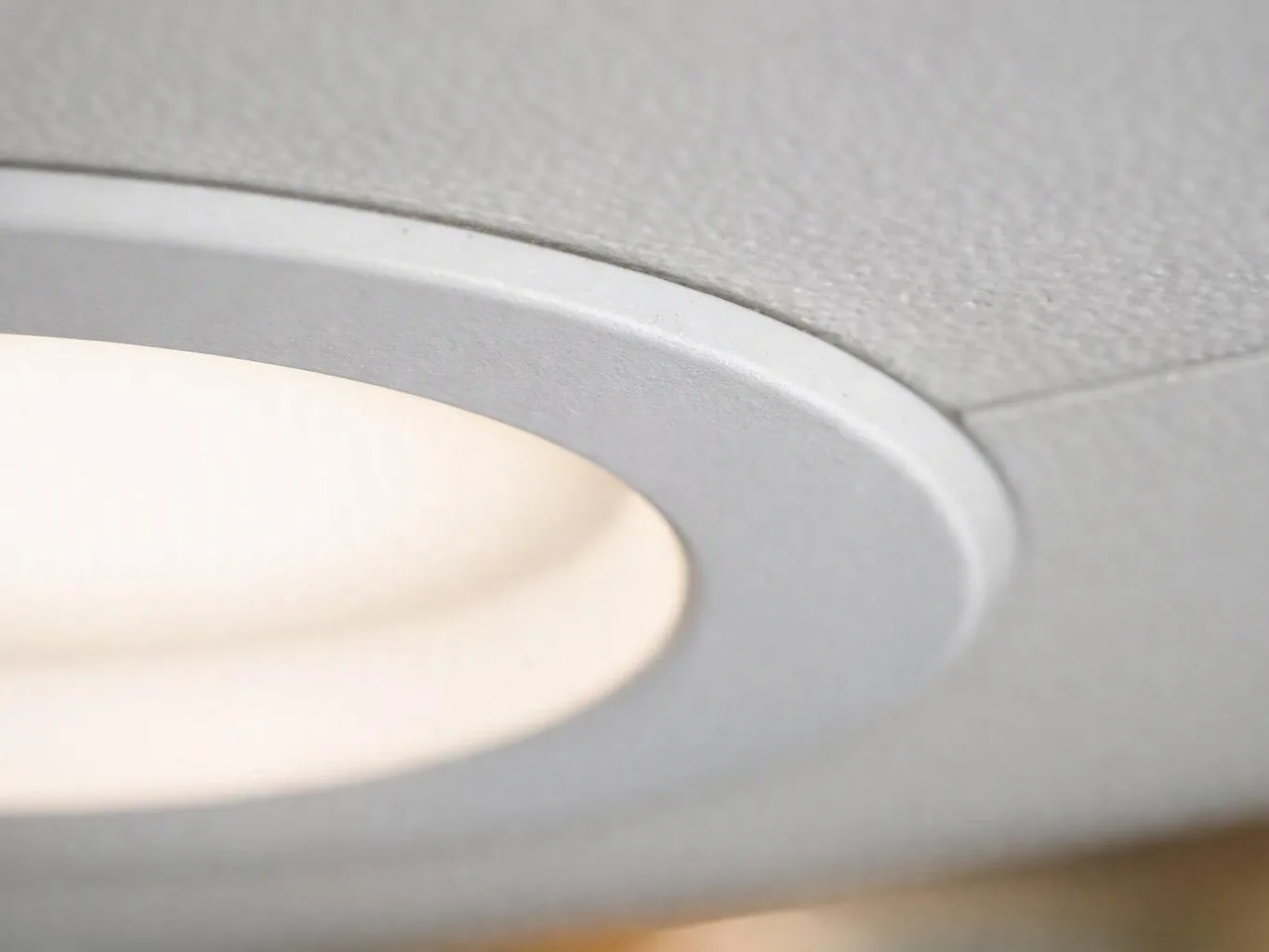 Close-up of a recessed ceiling light with a glowing white bulb in a gray fixture