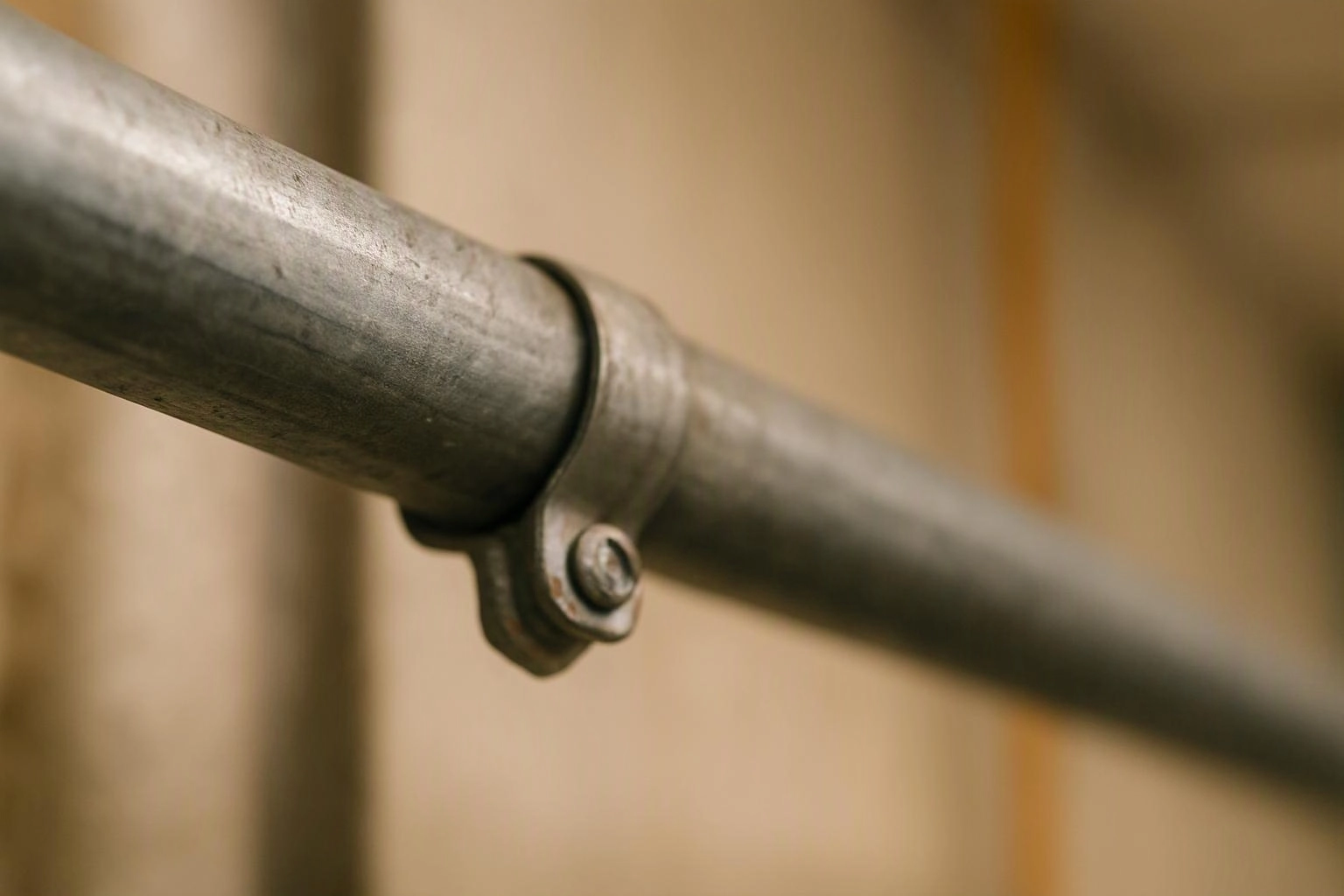 Close-up of a metal railing pipe with a clamp and bolt against a blurred beige background