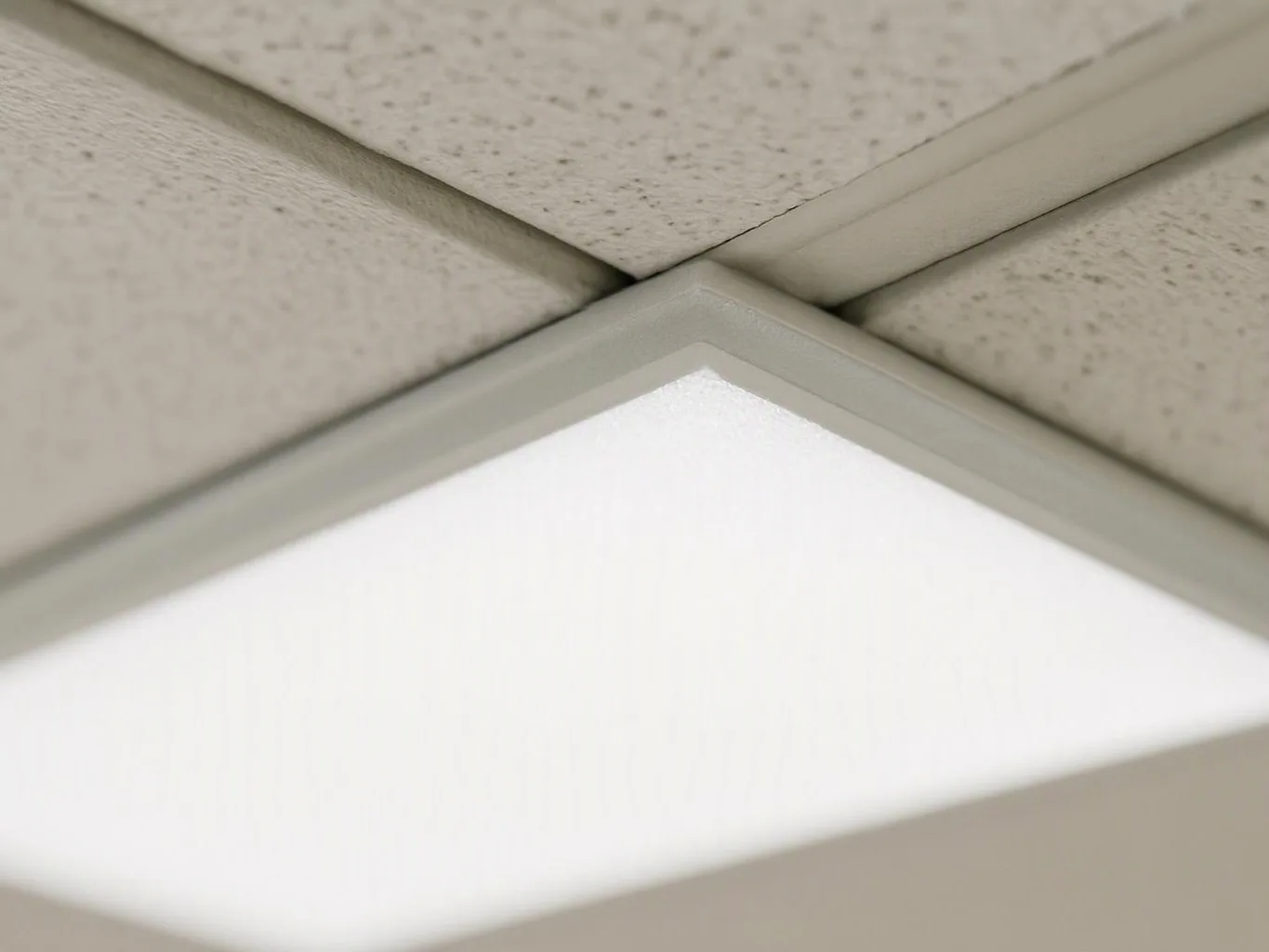 A recessed ceiling light glows beneath speckled acoustic tiles in a tiled ceiling grid
