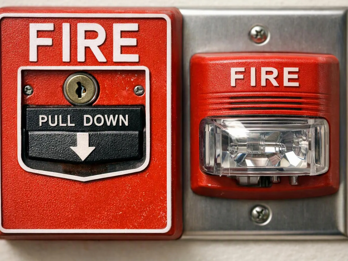 A red fire alarm pull station and strobe light are mounted on a metal wall plate