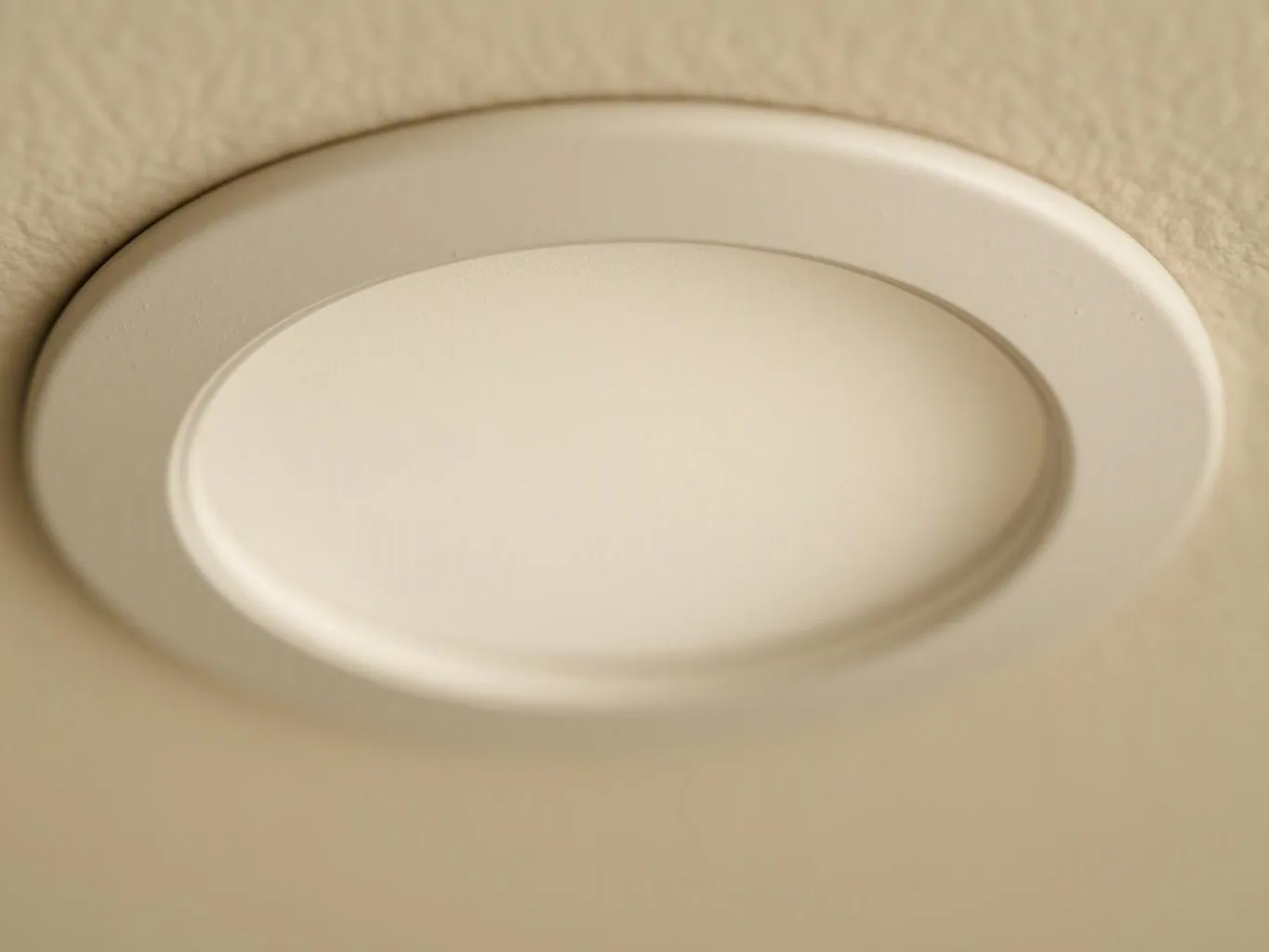 A round recessed ceiling light sits flush against a beige ceiling